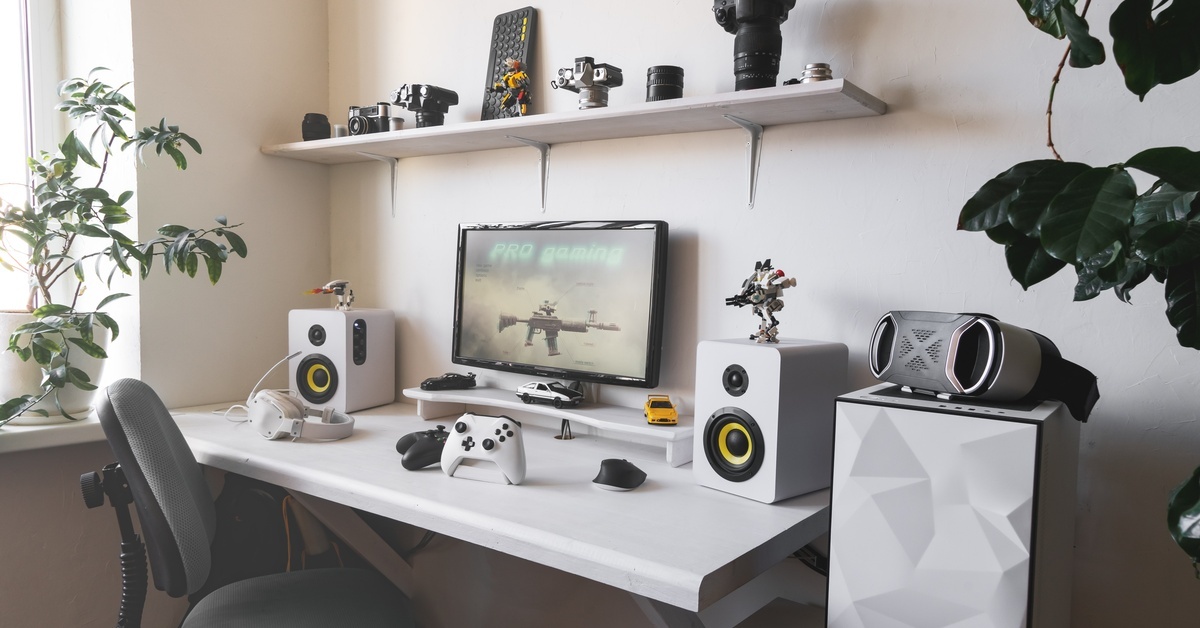 An all-white gaming setup on a white desk. There is a controller in front of a monitor depicting a video game gun.