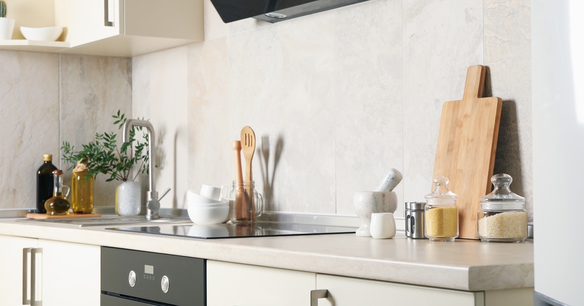 A modern kitchen interior with white cabinets and white countertops. There is a black stovetop with utensils on it as well.