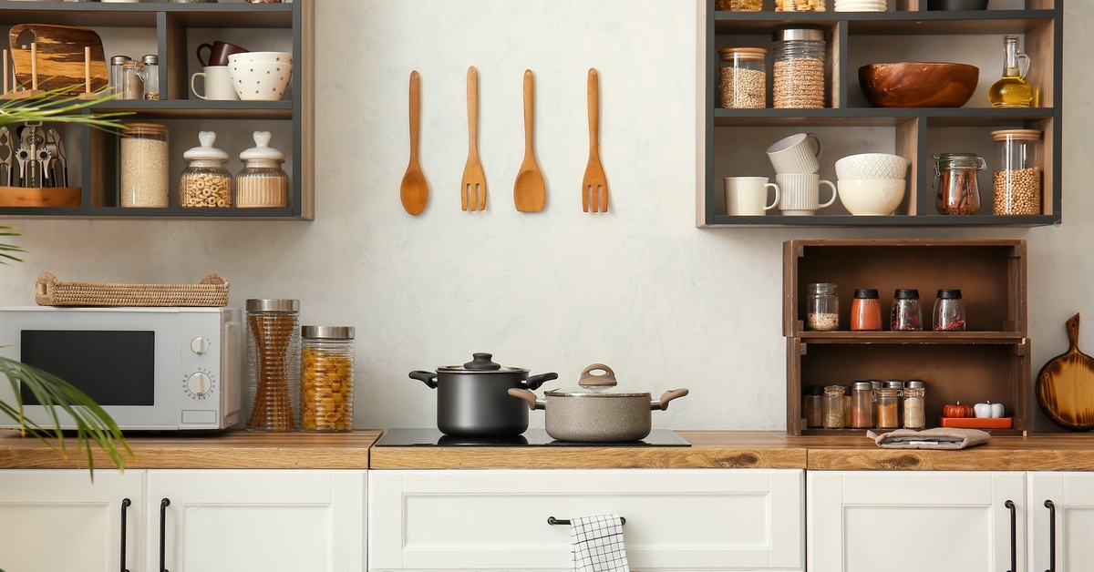 The interior of a modern kitchen with wooden countertops. Multiple shelves are full of kitchen supplies above the counter.