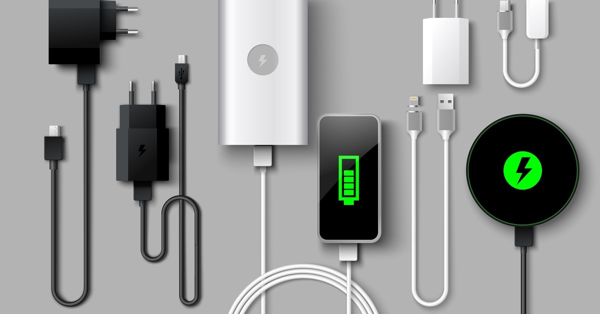 An array of different phone chargers laid out on a gray background. There are wired and wireless chargers.