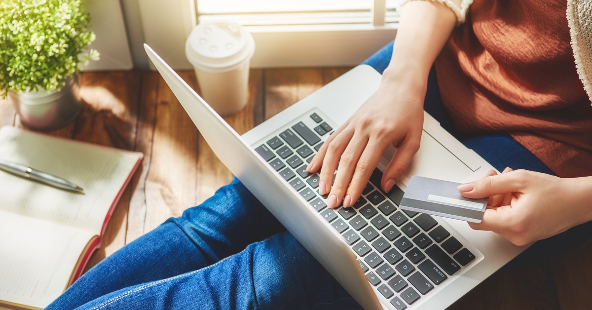 A woman sitting and looking at her laptop. She is holding a credit card in one hand with her other hand on the laptop.