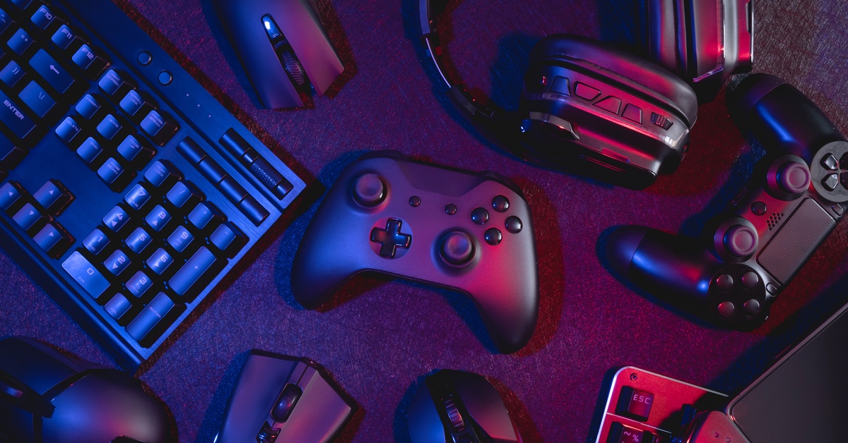 Several pieces of gaming paraphernalia on a black background. There are a few controllers and a keyboard and mouse.