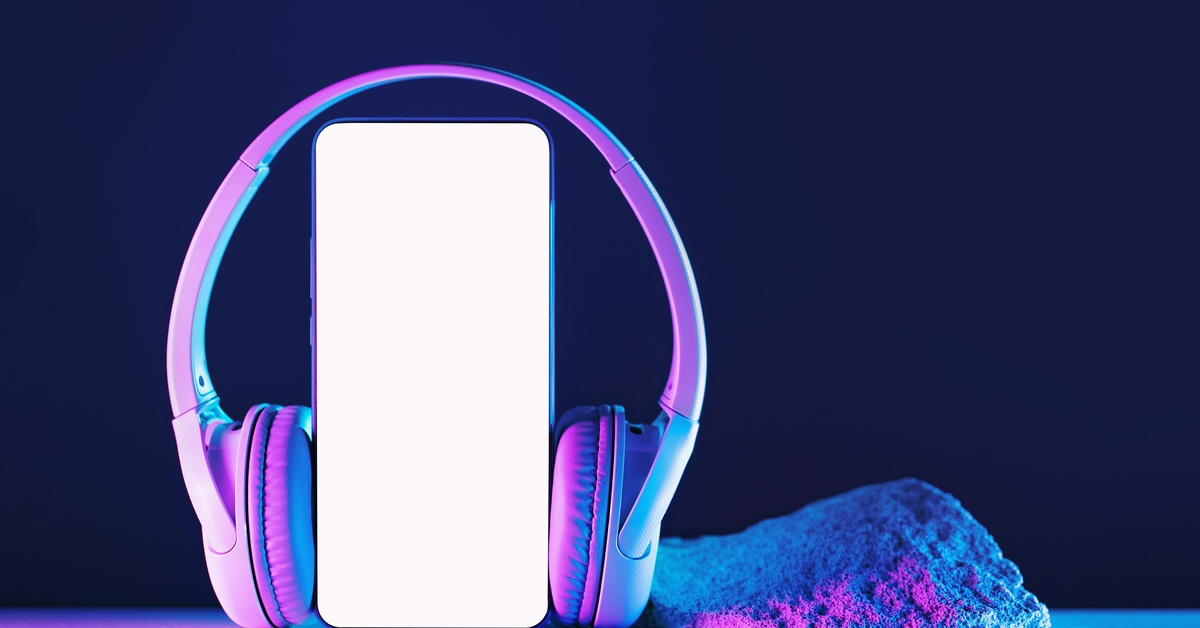 A pair of white headphones wrapped around a smartphone. The smartphone's screen is shining bright white.