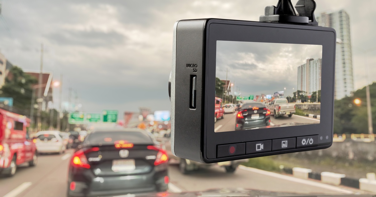 A dashboard camera in a car hanging from the windshield. The camera's screen is displaying the cars in front of it.