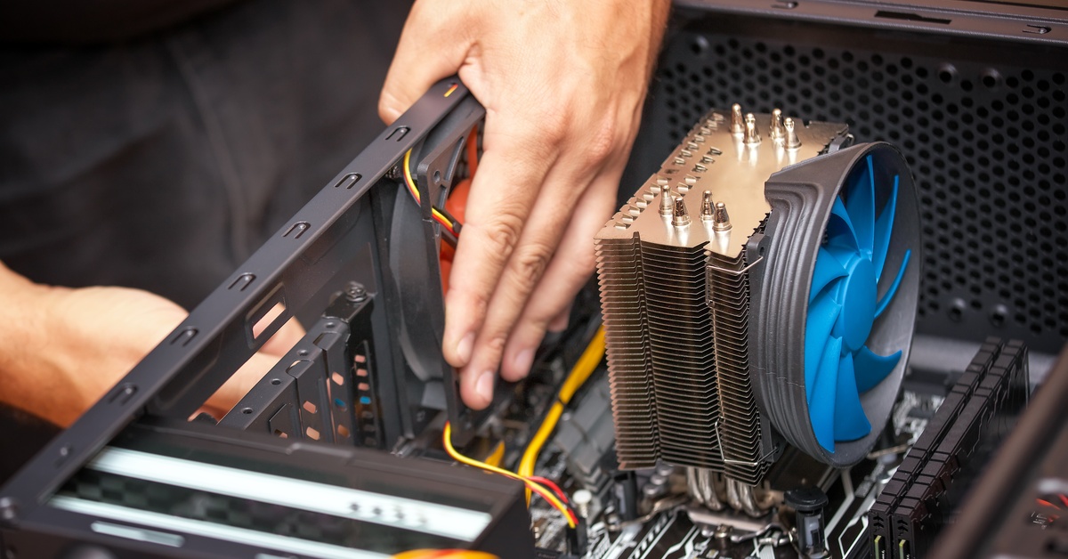 The hands of a computer technician reach into the case of a desktop computer to replace the cooling system.