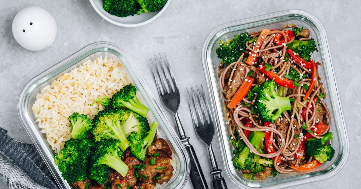 Two plastic containers full of a beef and broccoli stir fry meal. There are two forks in between the containers.