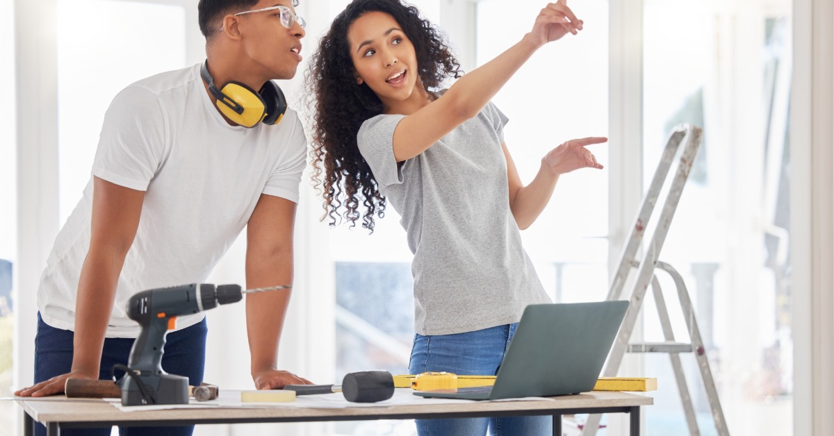 A man and woman standing in a half-finished room with tools around them. The woman is pointing off to the side.