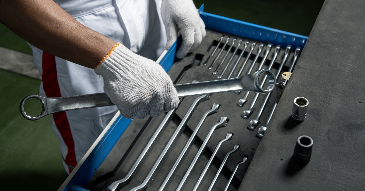 The gloved hands of a mechanic are pulling a large wrench out of a well organized tool box full of other wrenches.