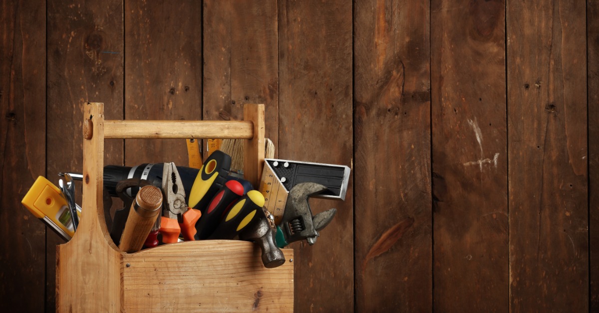 A small wooden tool box full of different kinds of tools. The tool box is sitting in front of a wooden background.