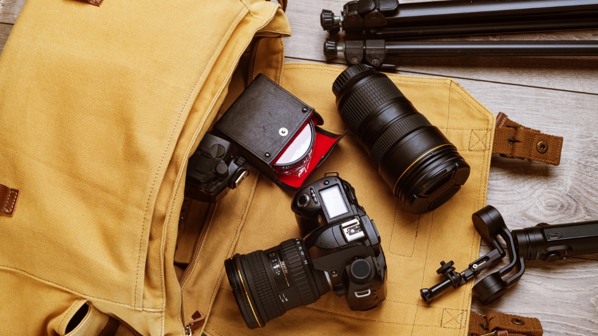 How To Avoid Overpaying for Digital Camera Accessories An open, tan camera bag spilling its contents on a table. The contents include a professional camera and lenses.