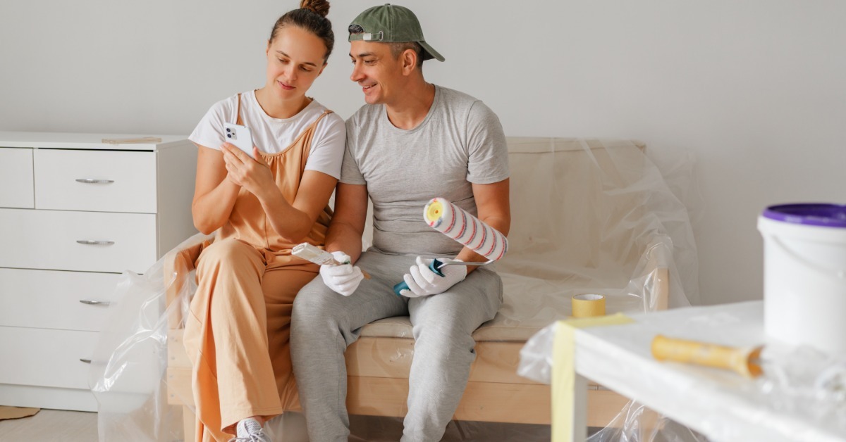 A man and woman in a living room putting together a dresser piece by piece. The pieces are laying all over the floor.